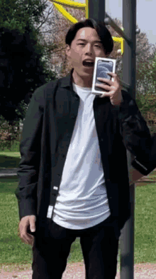 a man in a black shirt is holding a cell phone in his hand .