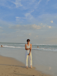 a man in white pants and a white tank top is standing on a beach