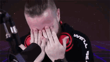 a man is covering his face with his hands in front of a microphone while wearing headphones .