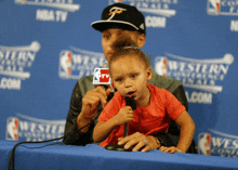 a little girl sits next to a man holding a microphone with nba tv on it