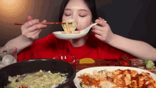 a woman is eating noodles with chopsticks from a spoon