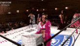 a woman in a pink dress stands in a wrestling ring with a sign that says u-next on it