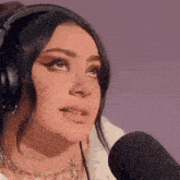 a woman wearing headphones and a necklace is crying in front of a microphone .
