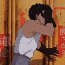a man in a white tank top is covering his face with his hand .
