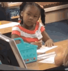 a little girl is sitting at a desk in a classroom with a name tag on her shirt .