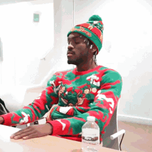 a man wearing an ugly christmas sweater sits at a table