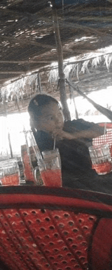 a young boy is drinking through a straw while sitting in a chair under an umbrella .