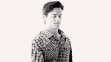 a man wearing a hat and a plaid shirt is standing in a black and white photo .