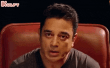 a man in a black shirt is sitting in a red chair making a funny face .