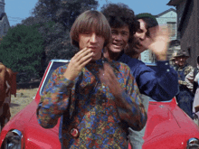 a man in a colorful shirt stands in front of a red car that says toyota
