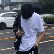 a man in a white t-shirt is standing in a parking lot with his head down