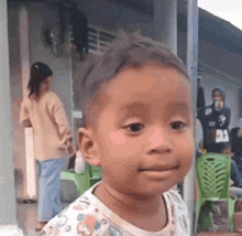 a little boy is smiling and looking at the camera while standing in front of a building .