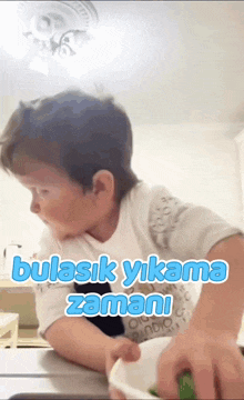 a young boy is playing with a bowl and the words bulasik yikama zamani are written above him