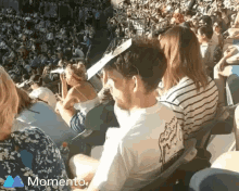 a man wearing a paper hat sits in a crowded stadium with the word momento on the bottom left