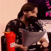 a man is sitting in front of a microphone holding a piece of paper and a red gatorade bottle