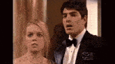 a man in a tuxedo and bow tie stands next to a woman in a dress