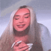 a woman with long blonde hair is holding a piece of paper in her hand and making a funny face .