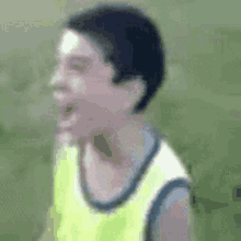 a young boy in a yellow vest is making a funny face while standing in the grass .