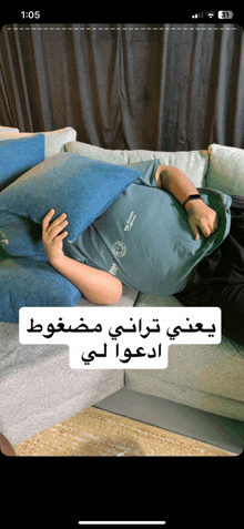 a man laying on a couch holding a blue pillow with the time 1:05 on the screen