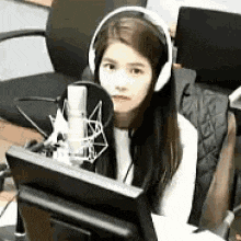 a woman wearing headphones is sitting in front of a microphone in front of a computer monitor .