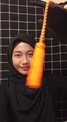 a woman wearing a black hijab is holding a yellow tassel