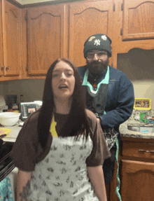 a man wearing a ny hat stands next to a woman in a kitchen