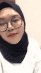 a woman wearing a hijab and glasses looks at the camera