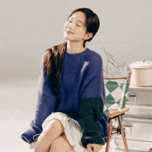 a woman in a purple sweater is sitting on a chair with her eyes closed