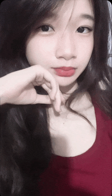 a girl with long black hair and red lips is making a heart shape with her hand
