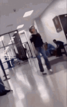 a woman is dancing in a hallway while a man sits on a bench in the background .