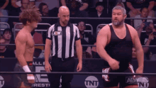 two wrestlers are standing next to each other in a ring with a referee and a sign that says aew on it