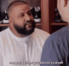 a man with a beard is talking to another man while wearing a white shirt .