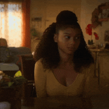 a woman in a yellow shirt is sitting at a table in a living room