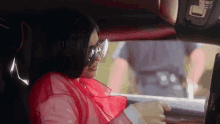 a woman wearing sunglasses and a red shirt is sitting in a car .