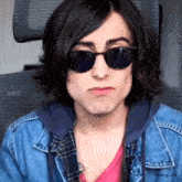 a young man wearing sunglasses and a denim jacket .