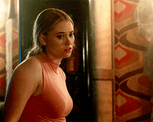 a woman in a pink tank top stands in front of a wall with a geometric pattern