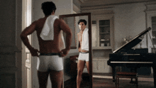 a man in underwear is looking at himself in a mirror in front of a piano