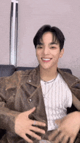 a young man wearing a brown leather jacket and a white striped shirt is smiling while sitting on a couch .