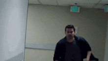 a man is running in a hallway with a green exit sign .
