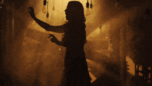a silhouette of a woman dancing in a dark room with lights hanging from the ceiling