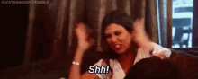 a woman is sitting on a couch with her fist in the air and says shh .