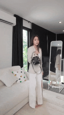 a woman standing in front of a mirror holding a small black bag with tiktok written on the bottom