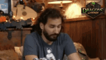 a man with a beard sits in front of a sign that says dragon and things