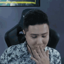 a man is sitting in a chair covering his mouth with his hand while playing a video game .