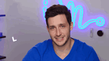 a man in a blue shirt is smiling in front of a neon sign that says ' n '