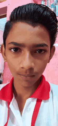 a boy wearing a white shirt with a red collar looks at the camera