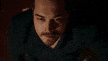 a close up of a man 's face with a mustache in a dark room .