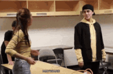 a man in a yellow hoodie is standing next to a woman in a yellow shirt in a classroom ..