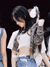 a woman wearing a white crop top and a camo jacket looks down