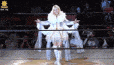 a woman in a white dress is standing in a wrestling ring with a revolution sign behind her